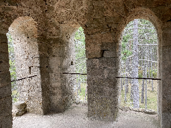 Ouvertures voûtées dans un mur ancien donnant sur un paysage boisé
